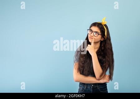 Pensive Indian teen girl dans l'habillement décontracté regardant l'espace de copie sur fond bleu de studio Banque D'Images