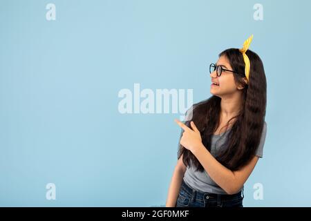 Une jeune fille indienne gaie pointant de côté à l'espace vide sur fond de studio bleu Banque D'Images