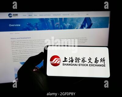 Personne tenant un téléphone portable avec le logo de la Bourse chinoise de Shanghai (SSE) sur l'écran devant la page web d'affaires. Mise au point sur l'affichage du téléphone. Banque D'Images