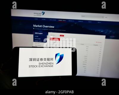 Personne tenant un téléphone portable avec le logo de la Bourse chinoise de Shenzhen (SZSE) à l'écran en face de la page Web d'affaires. Mise au point sur l'affichage du téléphone. Banque D'Images