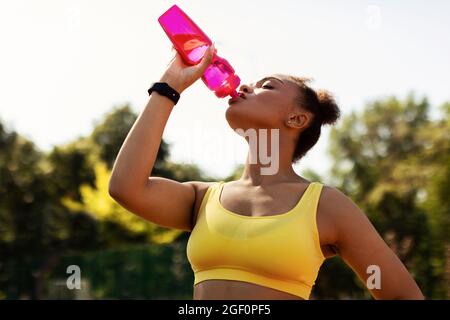 Portrait d'une femme noire sportive dans l'eau potable de sportswear jaune Banque D'Images