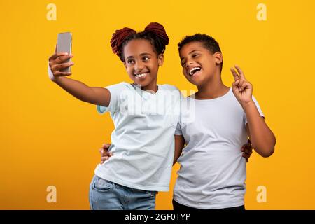 Des frères et sœurs noirs mignons qui se rassemblent sur leur téléphone portable Banque D'Images
