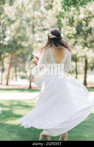 Belle mariée heureuse dans une robe de mariage blanche, tourbillons et danses dans le parc, belle mariée dans une robe de dentelle avec un bouquet, concept de mariage Banque D'Images