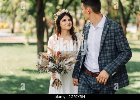 Mariage, jeune marié heureux et belle mariée tendre dans une robe de mariage avec un bouquet, mariée et marié tiennent les mains et marche sur un champ vert, mariage Banque D'Images