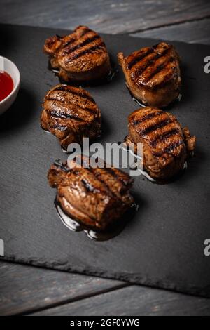 Médaillons de porc grillés au ketchup servis sur une table en bois sombre. Orientation verticale Banque D'Images