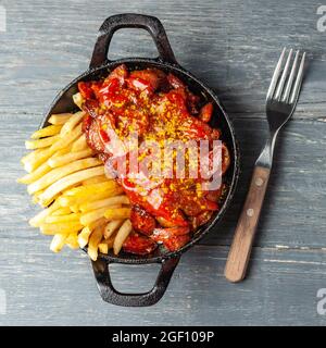 Currywurst avec des frites dans une casserole noire sur une table en bois. Banque D'Images