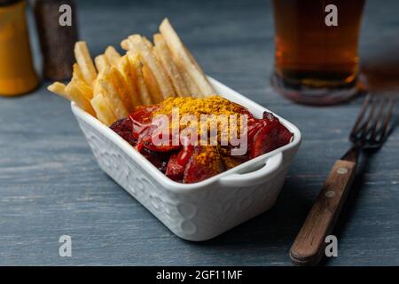 Currywurst avec des frites dans un bol blanc sur une table en bois. Banque D'Images