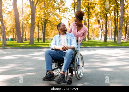 Une femme noire affectueuse et son petit ami handicapé en fauteuil roulant se regardant les uns les autres lors d'une promenade au parc en automne Banque D'Images