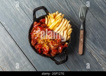 Currywurst avec des frites dans une casserole noire sur une table en bois. Vue de dessus. Banque D'Images