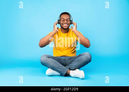 Black Guy écoutant de la musique avec les yeux fermés, fond bleu Banque D'Images