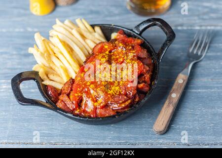 Currywurst avec des frites dans une casserole noire sur une table en bois. Banque D'Images