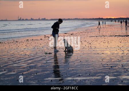 East Wittering, Sussex, Royaume-Uni, 22 août 2021 : à marée basse, les couleurs du ciel se reflètent le long de la plage de East Wittering Sussex. Alors que le temps est prévu pour se réchauffer pendant quelques jours, les habitants et les vacanciers ont profité de l'occasion pour nager, pêcher, jouer au cricket et marcher leurs chiens. À l'horizon lointain se trouve la Tour Spinnaker à Portsmouth. Anna Watson/Alay Live News Banque D'Images