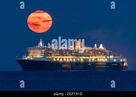 Weymouth, Dorset, Royaume-Uni. 22 août 2021. Météo Royaume-Uni. La pleine lune d'esturgeon s'élève dans le ciel nocturne presque clair de derrière le paquebot de croisière Cunard Queen Mary 2 qui est ancré dans la baie à Weymouth dans Dorset. Crédit photo : Graham Hunt/Alamy Live News Banque D'Images
