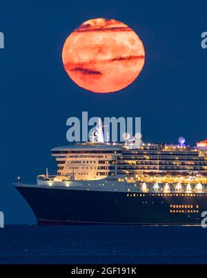Weymouth, Dorset, Royaume-Uni. 22 août 2021. Météo Royaume-Uni. La pleine lune d'esturgeon s'élève dans le ciel nocturne presque clair de derrière le paquebot de croisière Cunard Queen Mary 2 qui est ancré dans la baie à Weymouth dans Dorset. Crédit photo : Graham Hunt/Alamy Live News Banque D'Images