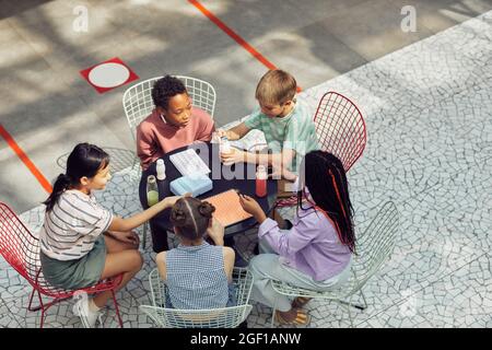 Vue en grand angle de divers groupes d'enfants assis à la table à l'extérieur pendant le déjeuner à l'école moderne, espace de copie Banque D'Images