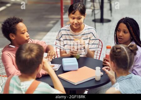 Portrait d'un groupe multiethnique d'enfants assis à la table à l'extérieur pendant le déjeuner à l'école moderne Banque D'Images