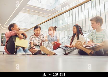 Portrait complet de divers groupes d'enfants assis sur le sol à l'école et bavardant dans le hall