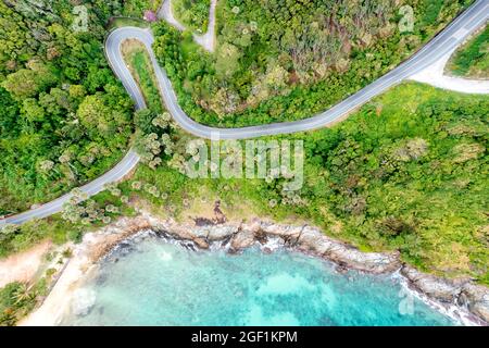 Drone aérien vue de dessus en bas des vagues se brisant dans le sable avec la route et la forêt. Vue panoramique sur la mer tropicale avec route en bord de mer. Phuket Thaïlande cur Banque D'Images