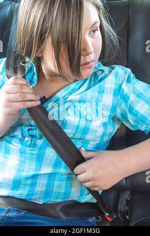 Blonde fille mettant une ceinture de sécurité dans le siège arrière d'une voiture Banque D'Images