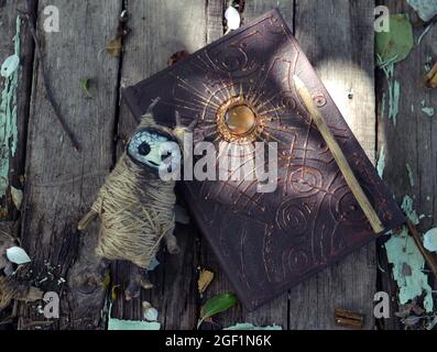 Livre magique avec couverture décorée et poupée voodoo sur planches dans le jardin à l'extérieur. Arrière-plan ésotérique, gothique et occulte, Halloween mystique et wicca co Banque D'Images