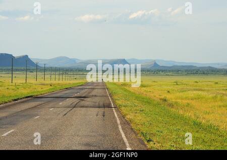 une route droite asphaltée à deux voies longe la ligne électrique à travers la steppe pittoresque jusqu'à la rencontre d'une chaîne de montagnes de forme inhabituelle. Kaki Banque D'Images