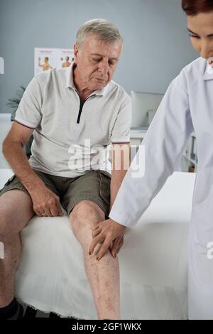 Physiothérapeute vérifiant la jambe blessée d'un patient âgé avant d'effectuer une physiothérapie dans un cabinet médical Banque D'Images