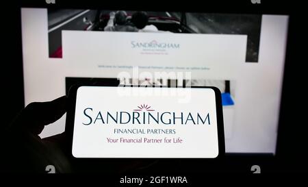Personne tenant un téléphone portable avec le logo de la société britannique Sandringham Financial Partners à l'écran en face de la page Web d'affaires. Mise au point sur l'affichage du téléphone. Banque D'Images