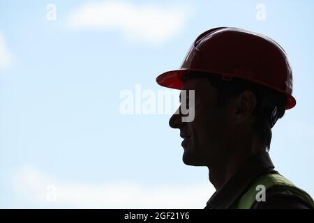 Portrait avec vue latérale rétroéclairé d'un ouvrier de la construction portant un casque tout en se tenant contre le ciel en arrière-plan, espace de copie Banque D'Images
