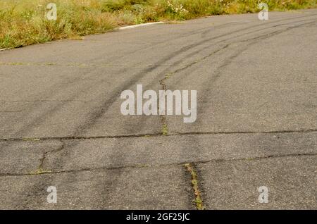 Asphalte gris avec chenilles noires pour pneus. Une vieille route de campagne avec des fissures. Herbe verte sur le côté de l'autoroute. La roue courbe suit un virage dans le dri Banque D'Images