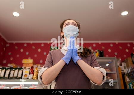 Les petites entreprises pendant la pandémie. Une travailleuse dans un masque médical et des gants en caoutchouc, la répand les mains et regarde avec espoir. Vue boom. Conce Banque D'Images