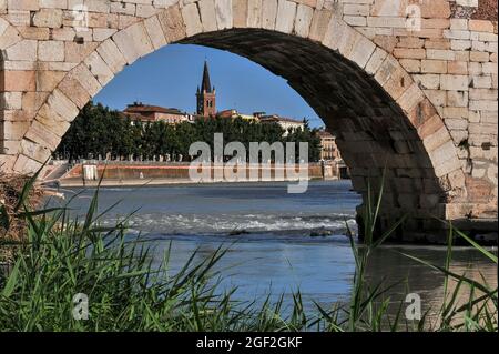 Le clocher et la flèche de l'église de San Tomaso Becket encadrés par une arche romaine reconstruite du Ponte Pietra, le plus ancien pont de Vérone, Vénétie, Italie. L'ancien Pons Marmoreus transporta l'importante via la route romaine de Postumia. Les Romains reconstruisirent la structure originale en pierre blanche, mais à l'époque médiévale, elle s'effondra souvent. En 1945, quatre des cinq arches du Ponte Pietra ont été rabâties par les forces allemandes, mais elles ont été reconstruites en 1957-9 en utilisant des centaines de blocs de pierre romains et de briques médiévales récupérés du lit de la rivière Adige qui coule rapidement. Banque D'Images