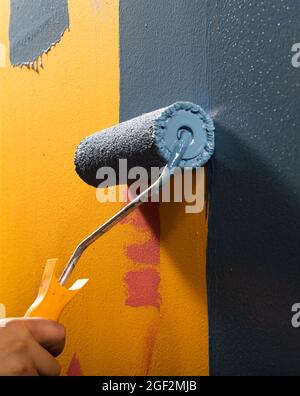 Peinture bleue humide sur un mur, avec une main, tenant un rouleau de peinture Banque D'Images