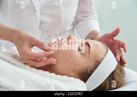 Jeune femme ayant un traitement d'acupuncture sur son visage dans le salon de spa. Médecine alternative et concept de thérapie Banque D'Images