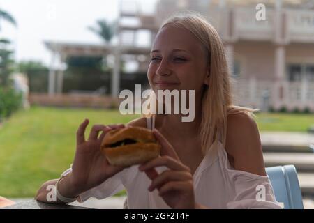 une adolescente mange un hamburger et rit. Banque D'Images