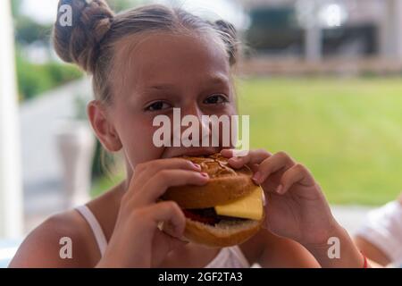 une adolescente mange un hamburger et rit. Banque D'Images