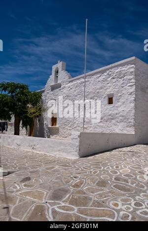 Ancienne petite chapelle avec arbres dans la cour destination religieuse à Kimolos île Chora Cyclades Grèce. Église orthodoxe blanchie à la chaux avec beffroi et croix e Banque D'Images