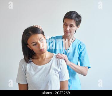 Médecin neurologue professionnel d'âge moyen examinant le cou d'une jeune femme africaine bouleversée Banque D'Images