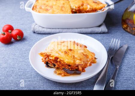 Moussaka avec viande, aubergine, tomates, pommes de terre, sauce au béchamel et fromage sur une assiette blanche. Cuisine grecque traditionnelle. Gros plan. Banque D'Images