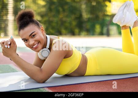 Femme sportive noire dans les vêtements de sport jaunes mentant et posant Banque D'Images