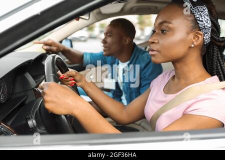 Femme noire concentrée pratiquant le stationnement à l'école de conduite Banque D'Images