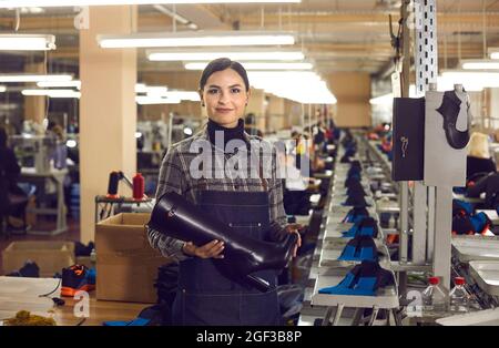 Une femme ravie à l'usine de chaussures qui tient une chaussure à talon pour femme de la nouvelle collection. Banque D'Images