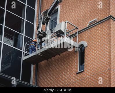 Réparer la façade du bâtiment en hauteur dans le berceau de levage. Ouvriers de construction en hauteur travaillant sur une grue dans un godet de levage. Banque D'Images