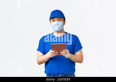 Achat en ligne, covid-19, prévention des virus et concept de livraison. Jeune coursier asiatique souriant dans un masque médical et des gants vérifiant l'adresse ou le client Banque D'Images