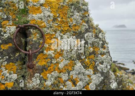 Un vieux bateau circulaire en fer rouillé sur des roches couvertes de lichen dans les Shiant Isles. Galtachanan en arrière-plan. Banque D'Images