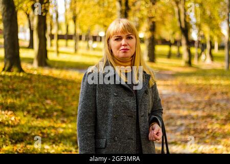 Flou artistique en extérieur portrait d'une femme mature positive et confiante. Blonde femme souriante. Élégante femme d'âge moyen dans le parc d'automne. Hors foyer Banque D'Images