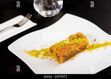 Dessert Kadayif avec pistache sur une assiette en porcelaine blanche. Banque D'Images