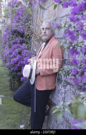 Beau modèle mâle gris-cheveux posant contre un mur avec des fleurs de bougainvilliers Banque D'Images