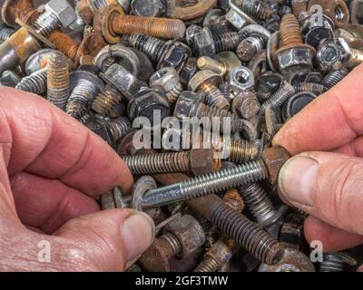 Gros plan de dessus de POV de mains d'un homme fixant un écrou à un boulon et une rondelle, de l'assortiment aléatoire empilé derrière. Banque D'Images