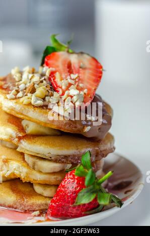 Crêpes empilées de bananes, fraises et noix, nappées de chocolat et de sauce aux fraises, petit déjeuner sucré Banque D'Images