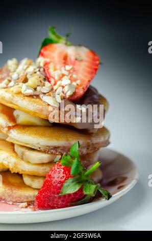 Crêpes empilées de bananes, fraises et noix, nappées de chocolat et de sauce aux fraises, petit déjeuner sucré Banque D'Images